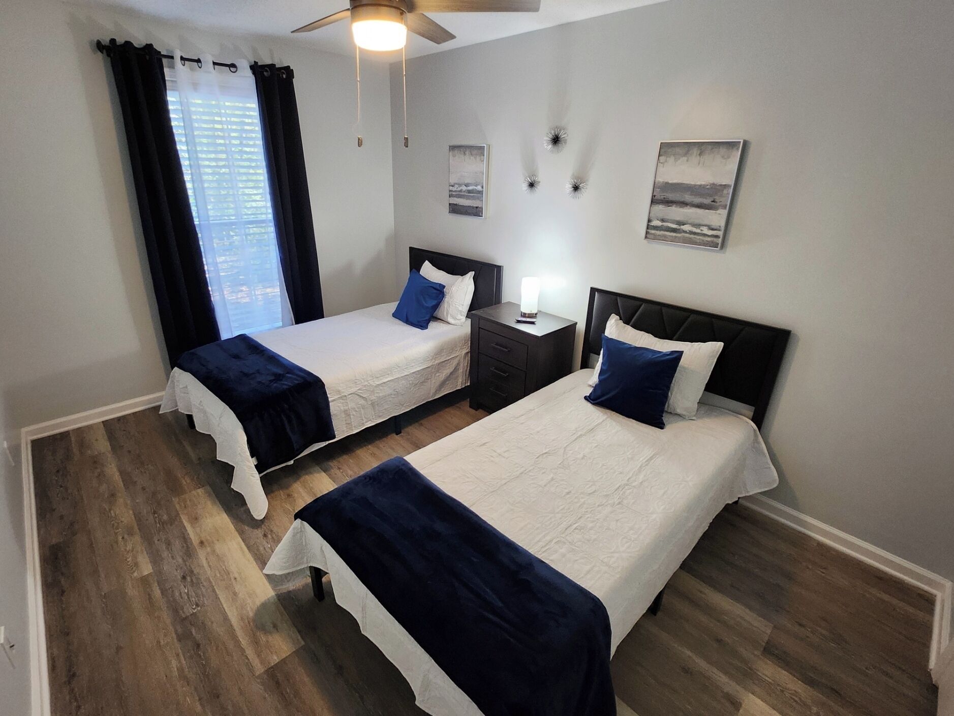 Een hotelkamer met twee bedden, een plafondventilator, een nachtkastje en kunst aan de muren.