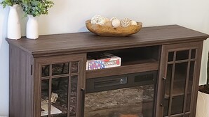 Un meuble en bois foncé doté de portes en verre, un bol décoratif posé sur le dessus et une boîte étiquetée « CONNECT 4 » sur l’étagère inférieure.