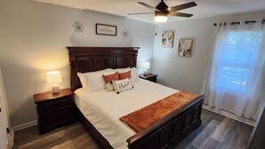 Une chambre à coucher avec un lit en bois, deux tables de chevet avec des lampes, un ventilateur de plafond et des œuvres d’art accrochées aux murs.