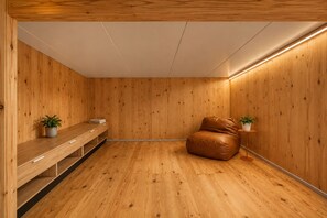A room with wooden walls and flooring, a leather sofa, a wooden bench with a plant, and a small table with a plant.