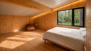 A bedroom with a wooden ceiling, a large window with a view of trees, a bed, and a brown leather chair. - Wabi Sabi at The Retreat at Water's Edge (Tracy City)