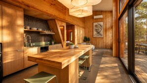 A modern kitchen with wooden cabinetry, a central island with bar stools, and a large window providing a view of the outdoors. - Wabi Sabi at The Retreat at Water's Edge (Tracy City)