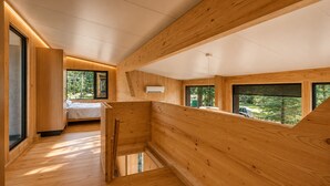 Un intérieur moderne avec des lambris en bois, un lit et de grandes fenêtres donnant sur l’extérieur.