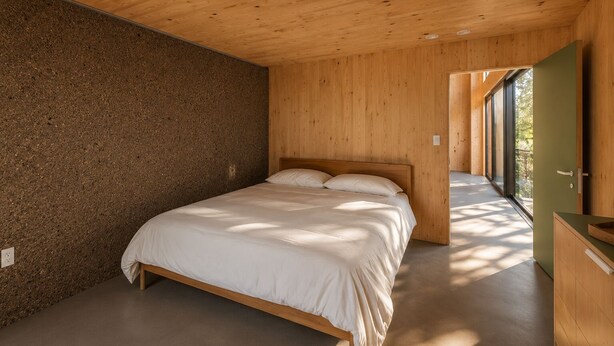 Une chambre avec un lit en bois, un plancher en béton et un mur vert.