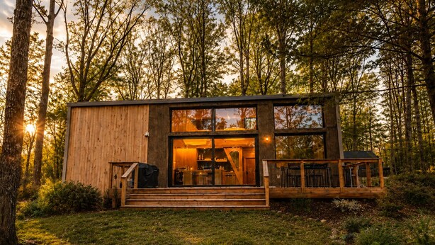 A modern wooden cabin with a glass facade, a deck, and a staircase leading to the entrance. - Wabi Sabi at The Retreat at Water's Edge (Tracy City)