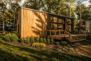 A wooden cabin with a deck, surrounded by trees and greenery.