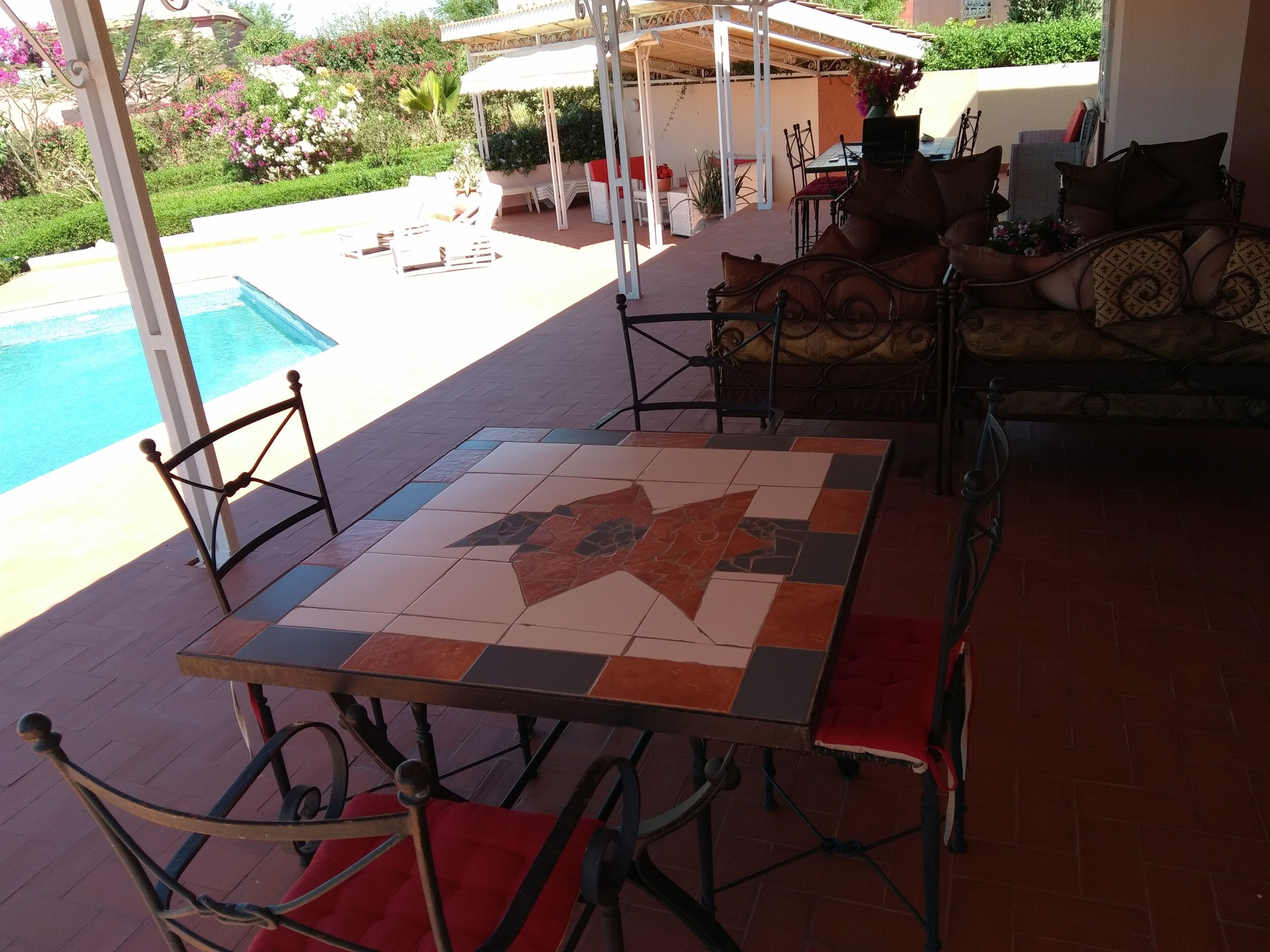 A patio area with a tiled table and chairs, a pool, and outdoor furniture.