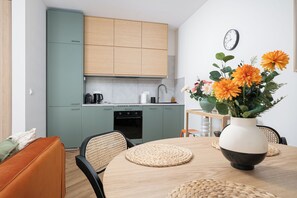 A modern kitchen with light green cabinets, a wooden dining table with woven placemats, and a vase with flowers. - RentPlanet - przy Dworcu Centralnym (Warsaw)