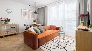 A modern living room with a sofa, a small table, a cabinet, and a large window with curtains. - RentPlanet - przy Dworcu Centralnym (Warsaw)