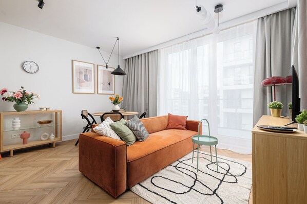 A modern living room with a sofa, a small table, a cabinet, and a large window with curtains. - RentPlanet - przy Dworcu Centralnym (Warsaw)