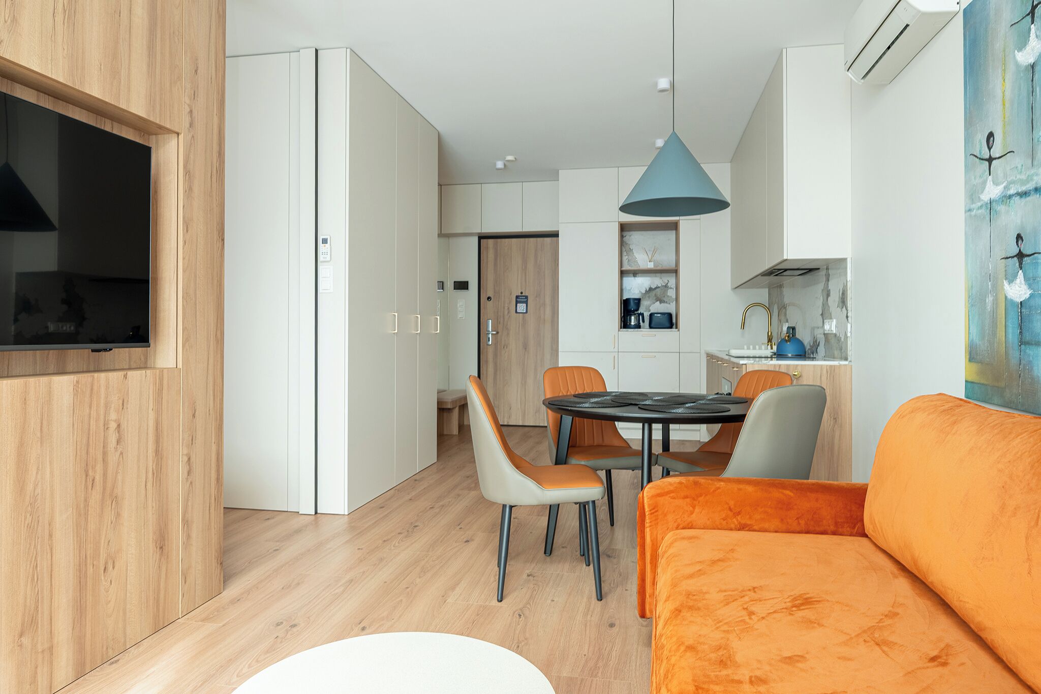 Un salon moderne avec un téléviseur, un canapé orange et un coin repas comprenant des chaises et une table.