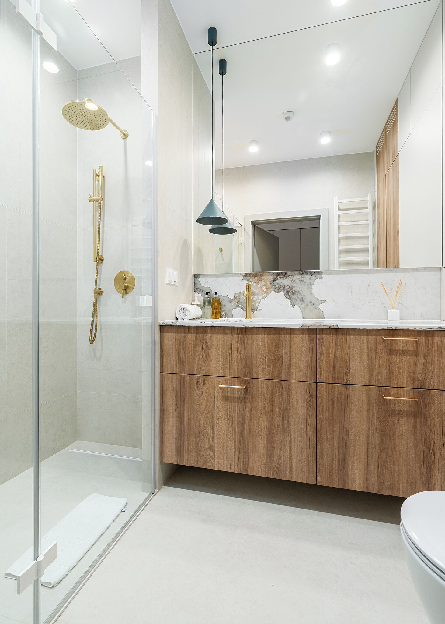 A modern bathroom with a glass shower enclosure, a gold showerhead, and a wooden vanity with a marble countertop.