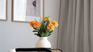 A bed with a green pillow, a white vase with orange flowers, and a wicker chair. - RentPlanet - przy Dworcu Centralnym (Warsaw)