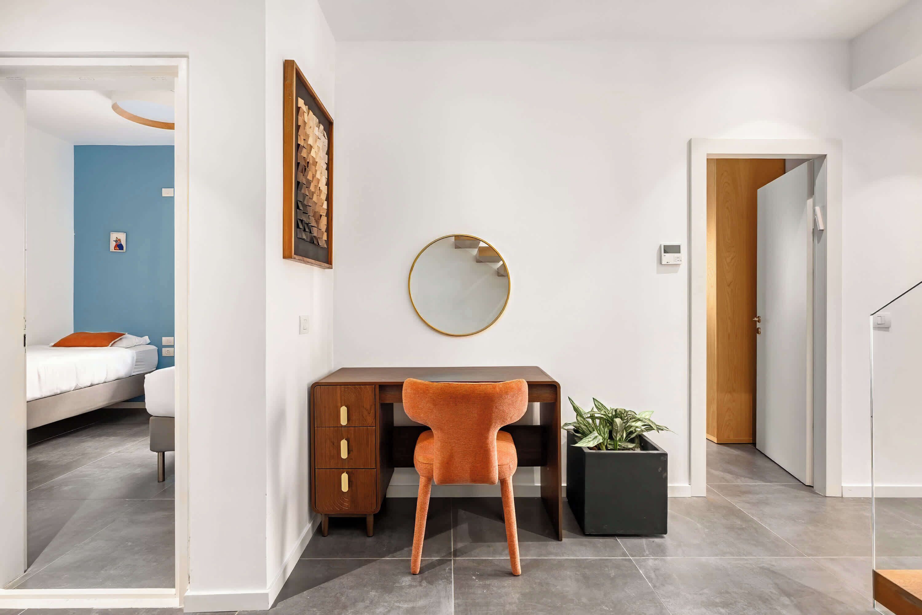 Een moderne slaapkamer met een bed, een bureau en een stoel. Er hangt een spiegel aan de muur en op het bureau staat een pot met een plant.