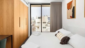 Une chambre d’hôtel avec un grand lit, une armoire en bois, un balcon donnant sur la ville et un tableau au mur.
