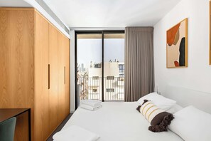 A hotel room with a large bed, a wooden wardrobe, a balcony with a view of the city, and a painting on the wall. - Modern Duplex 4BR by the beach by HolyGuest (Tel Aviv-Yafo)