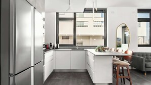 Une cuisine moderne avec un îlot central, une grande fenêtre et un canapé gris dans l’espace salon.