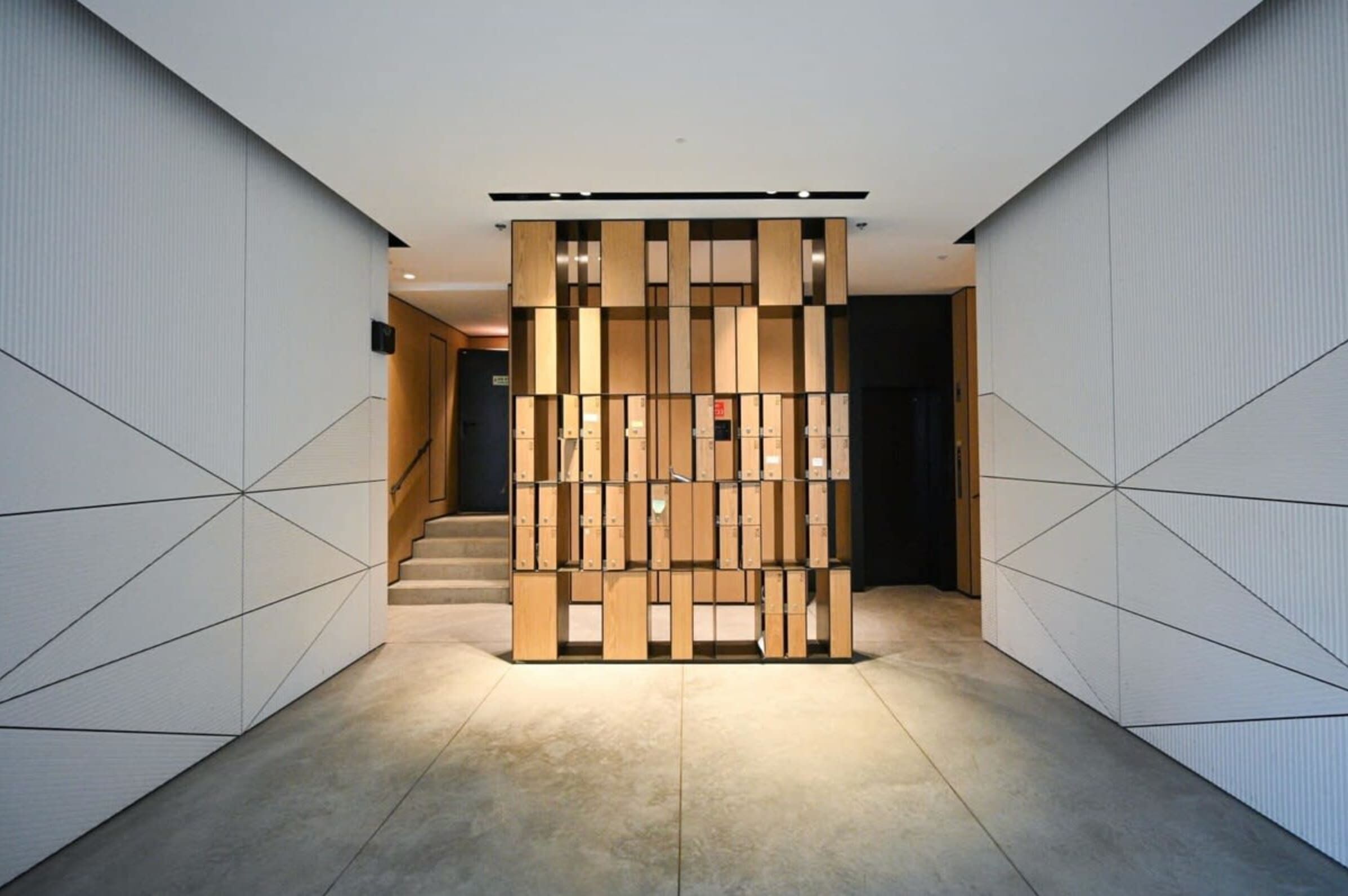 A modern hallway with a geometric wall design, a central wooden partition, and a staircase leading to another area.