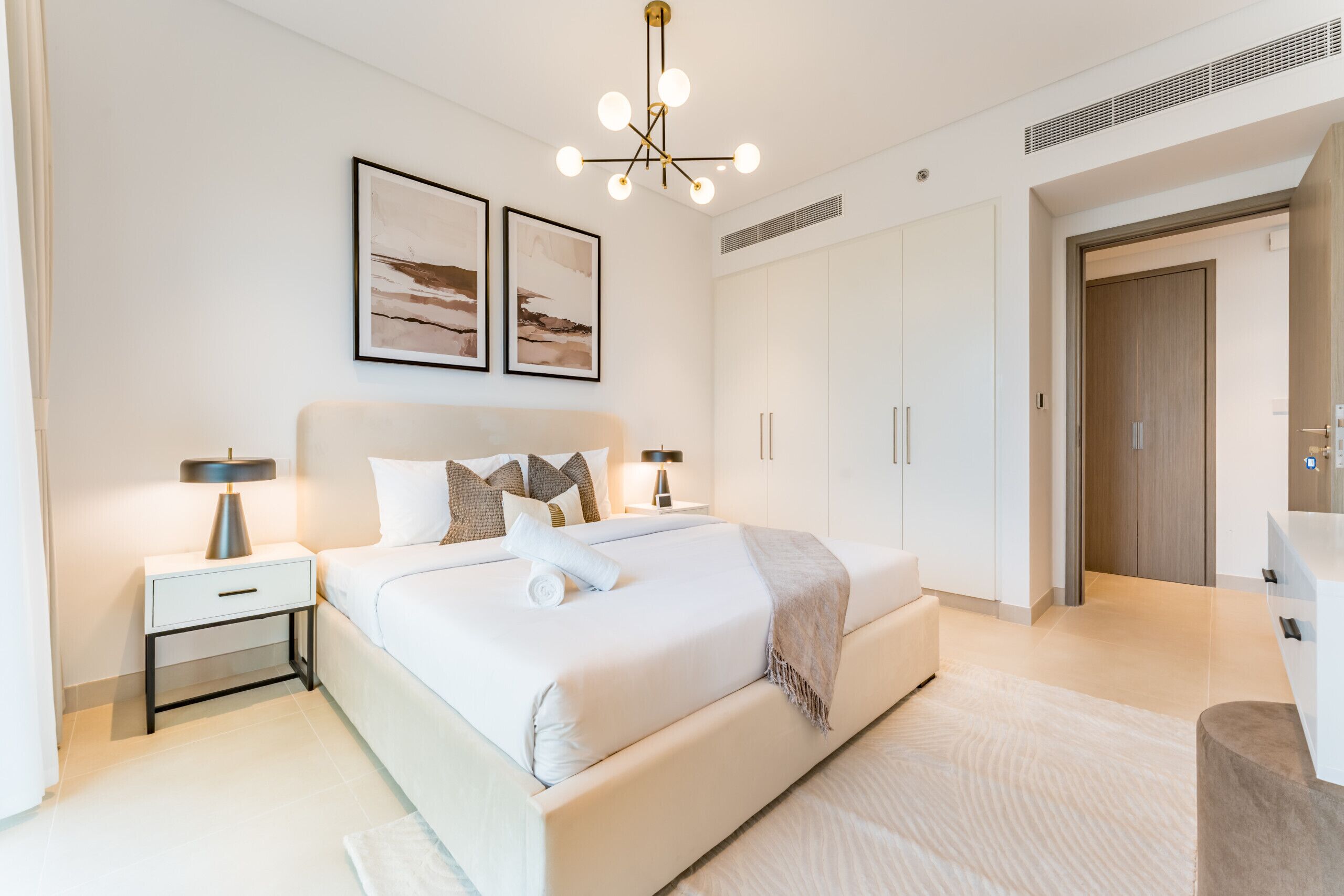 A modern bedroom with a large bed, bedside tables, a ceiling light fixture, and a wardrobe.