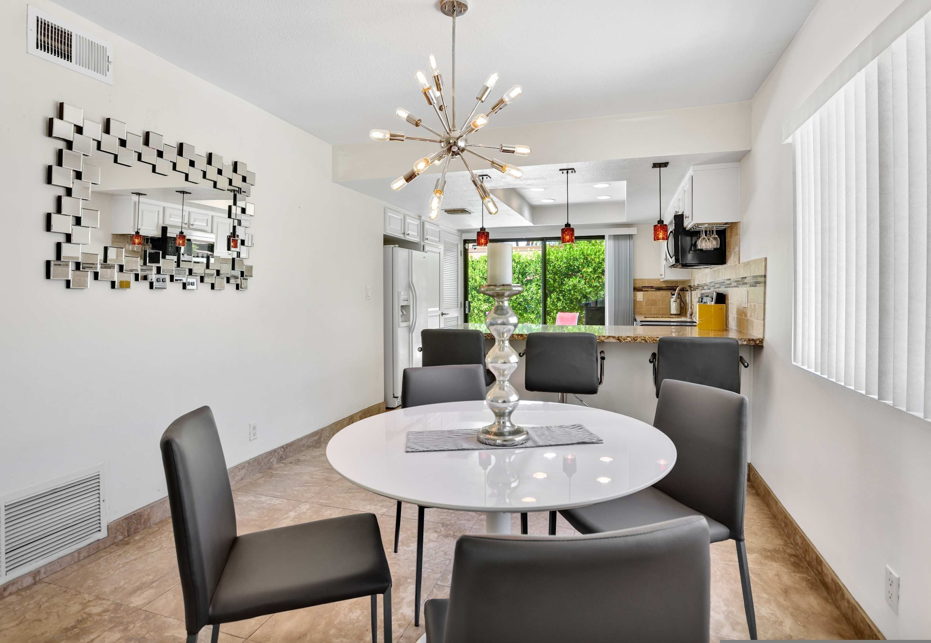 A modern dining area with a round table, six chairs, a decorative mirror, and a unique chandelier.