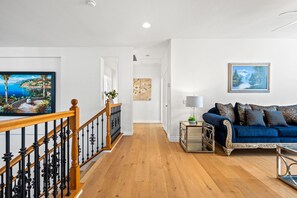 A living room with a blue sofa, wooden flooring, and a staircase with black railings. - Luxury Hilltop Home Spacious Private Backyard (Rowland Heights)