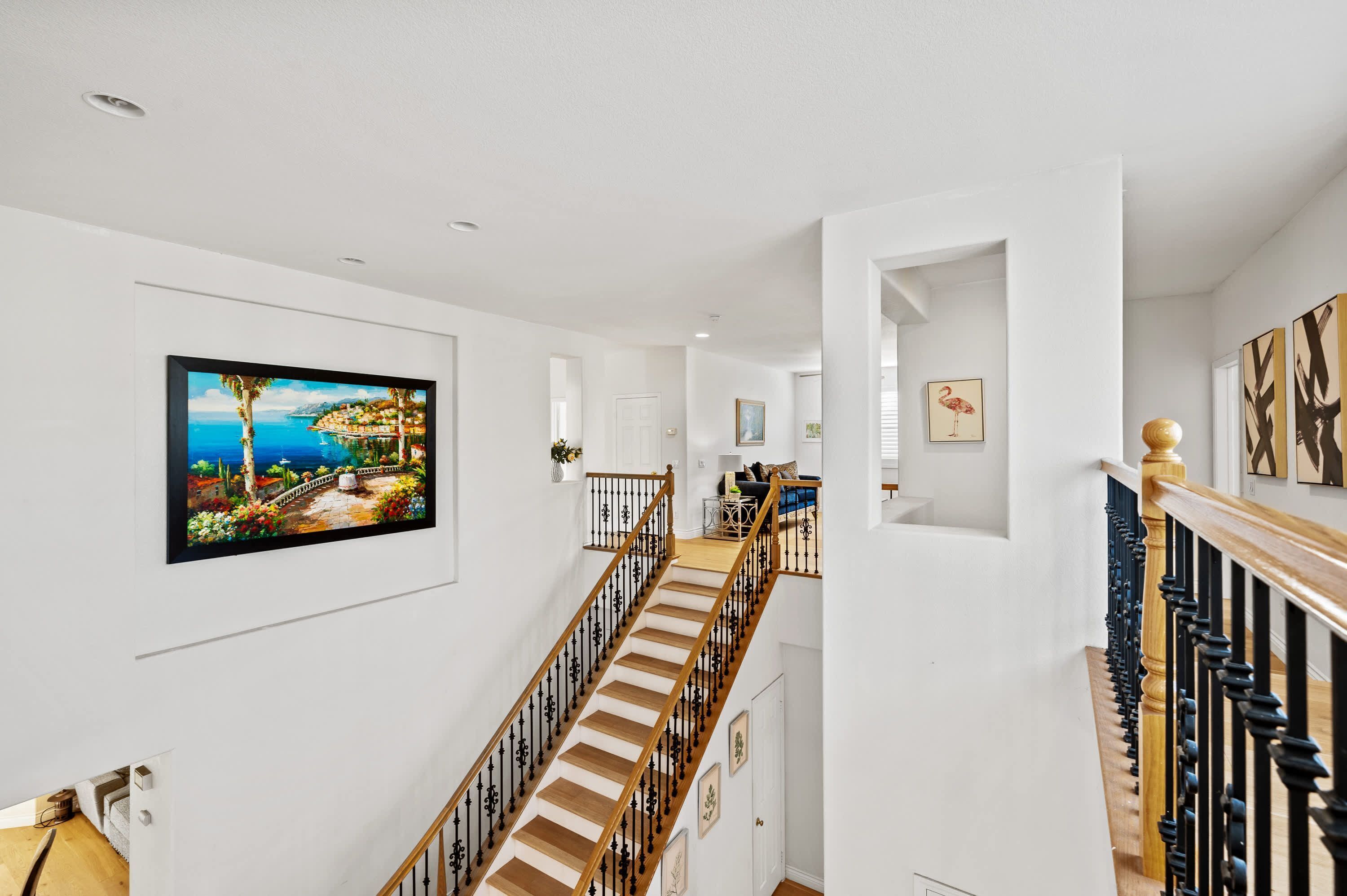A staircase with wooden steps and black balusters, leading to a landing with a white wall and a framed picture.