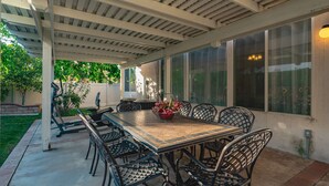 Une terrasse couverte avec une table en bois et des chaises en métal, entourée de grandes fenêtres.