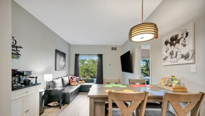 Ein modernes Wohnzimmer mit einer Couch, einem Esstisch mit Stühlen, einer Küchenzeile und einem großen Fenster mit Vorhängen.