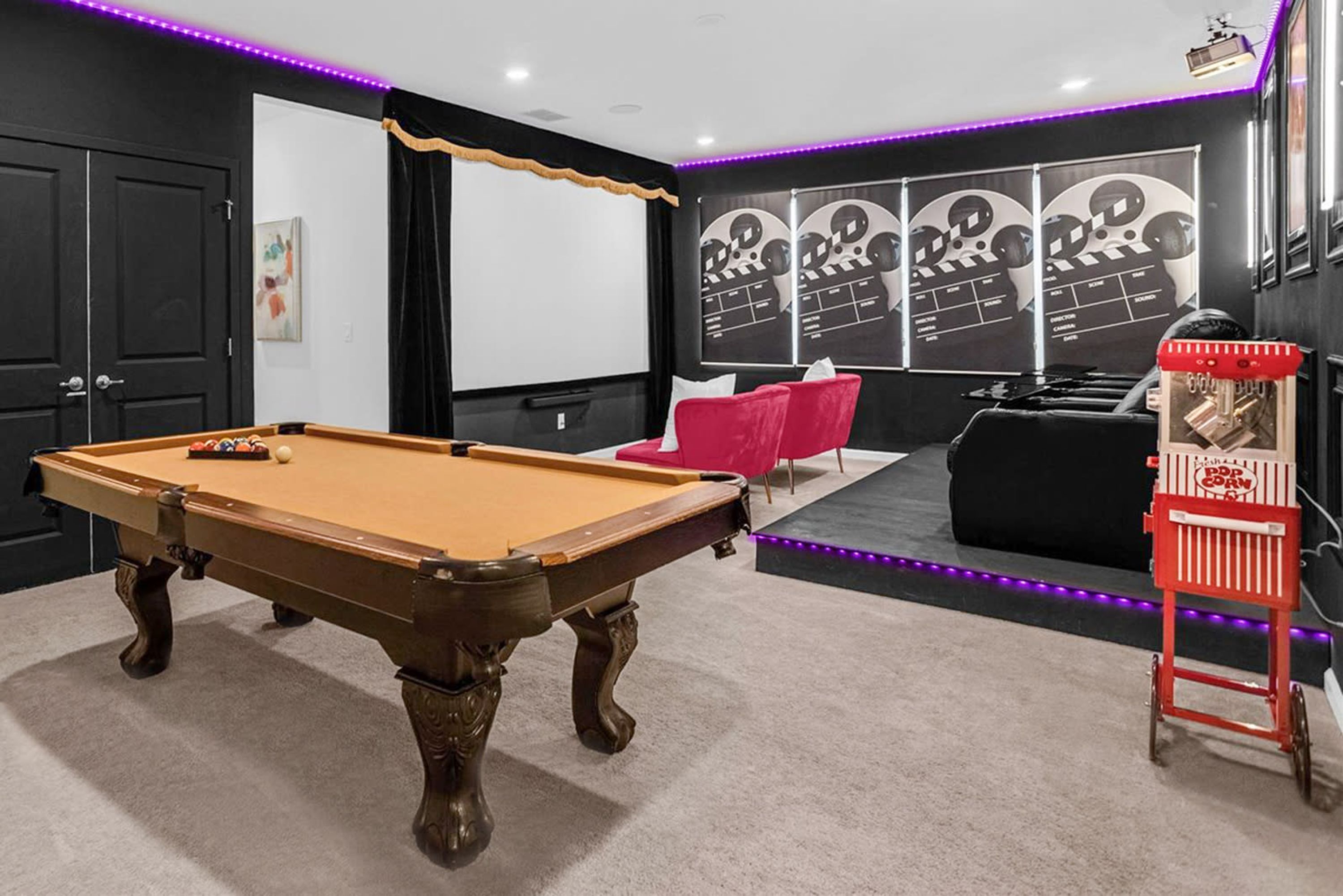 A pool table in a room with a black and white color scheme, a red chair, and a popcorn stand.