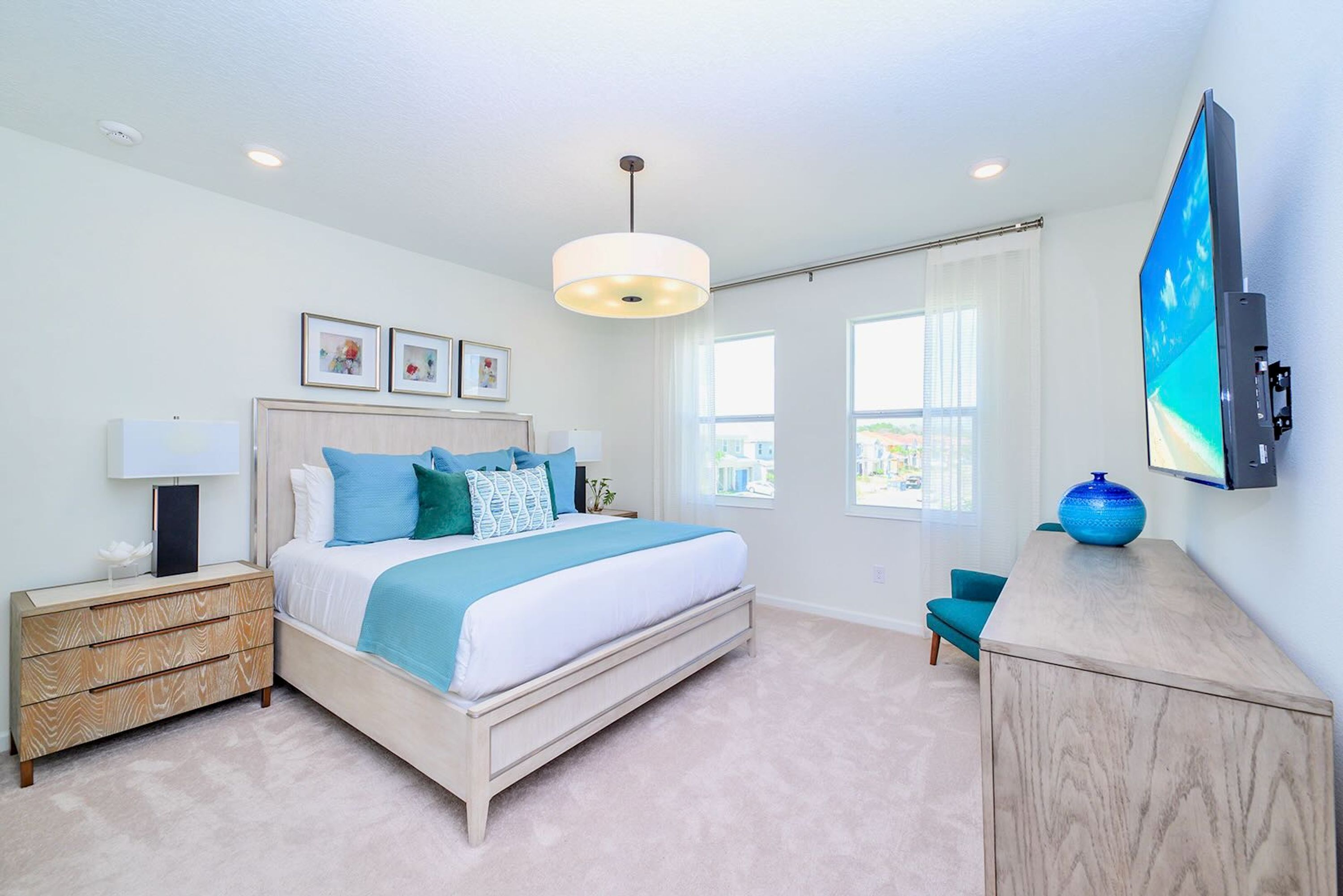 A modern bedroom with a bed, bedside tables, a TV, and a view of the outside.
