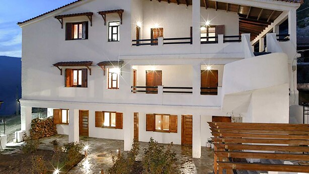 A two-story white building with multiple balconies and windows, featuring a wooden deck and outdoor seating area. - Goura Guesthouse Garden Double Room Lake Doxa (Sikyona)