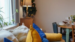 A cozy living room with a sofa adorned with colorful cushions, a Christmas tree, and a painting on the wall. - Coppet Cove 2 Bedroom Apartment - Tenby (Saundersfoot)