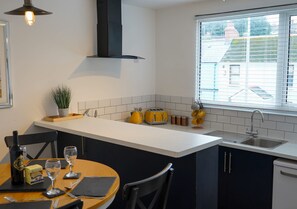 A modern kitchen with a white countertop, black cabinets, a built-in oven, and a window with blinds. - Ivy Cellar With 2 Bedrooms and 1 Bathrooms (Tenby)