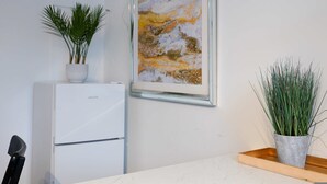 Keittiössä on valkoinen jääkaappi, kehystetty abstrakti maalaus ja kaksi ruukkukasvia.