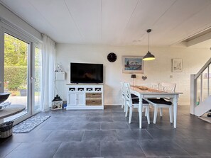 Ein modernes Wohnzimmer mit Flachbildfernseher, weißen Möbeln und einem Esstisch.