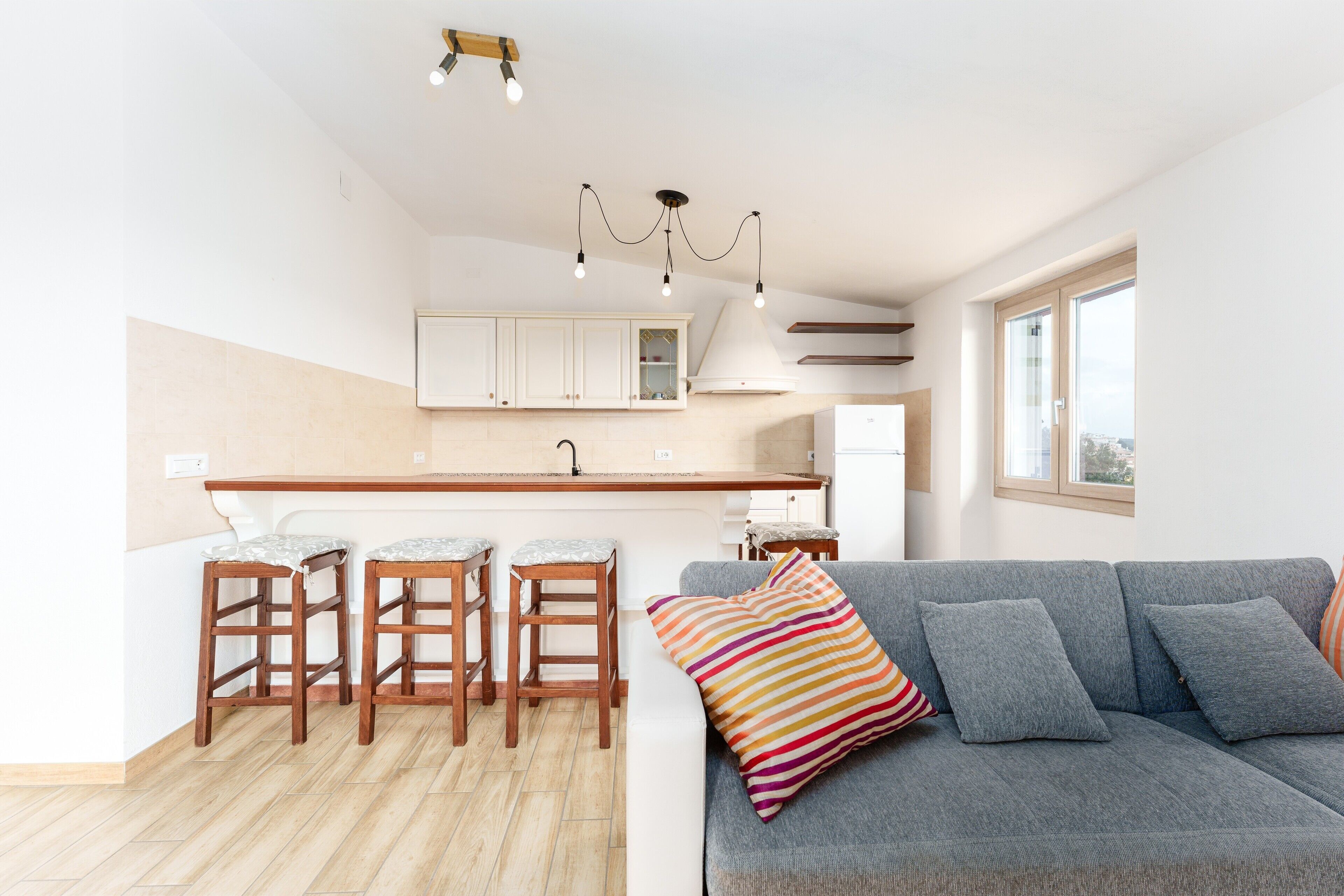 A modern kitchen with a central island, bar stools, and a grey sofa with striped cushions.