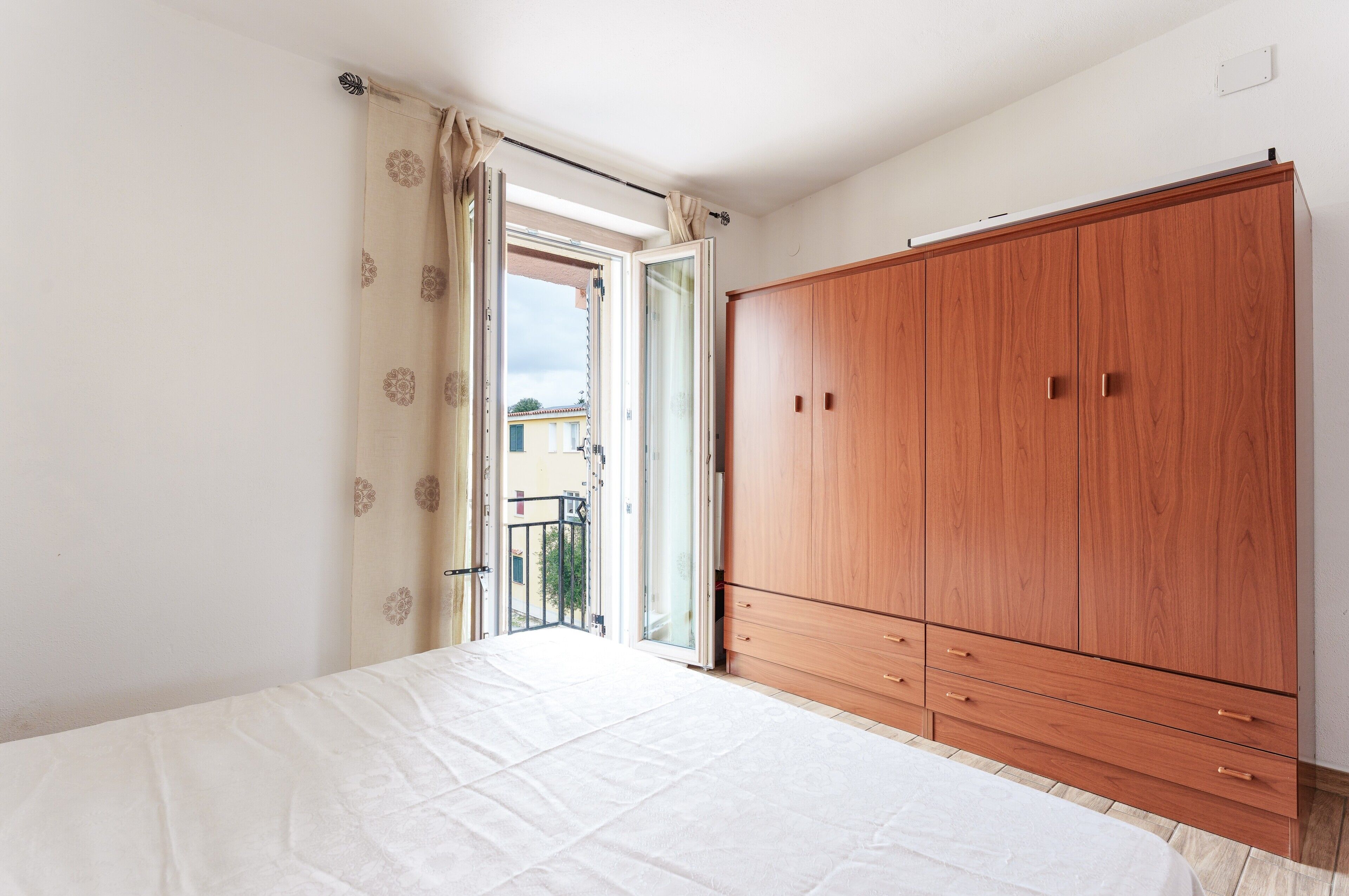 A bedroom with a bed, a wooden wardrobe, and a sliding glass door leading to a balcony.