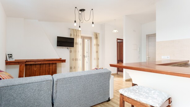 Een moderne woonkamer met een grijze bank, een houten tafel en een aan de muur bevestigde televisie.