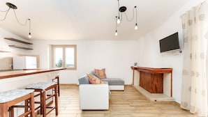 Een moderne woonruimte met een keuken, een zithoek met een bank en poef, een houten bar en een flatscreen televisie aan de muur.