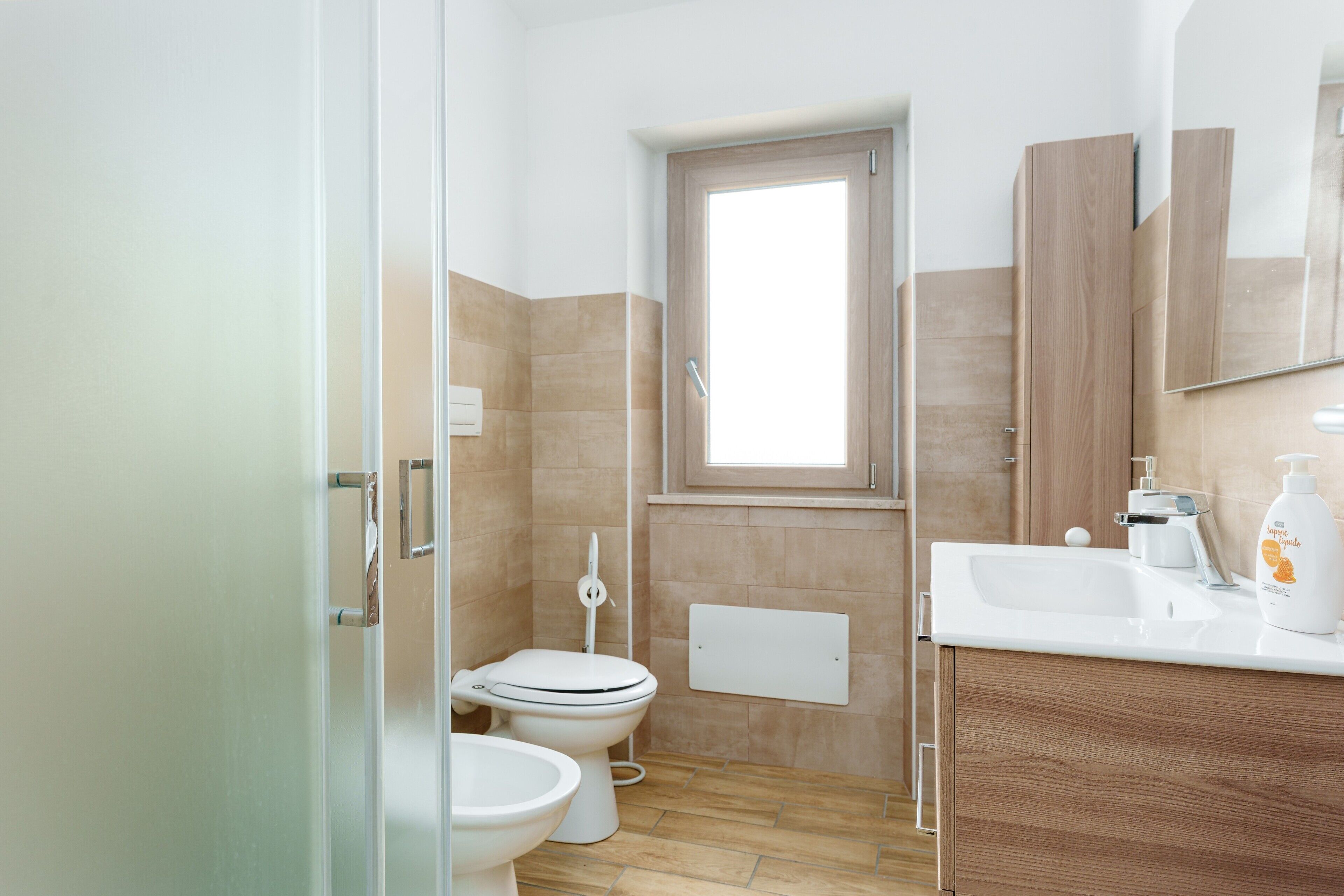 Une salle de bain avec deux toilettes, un lavabo, un miroir et une fenêtre.