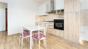 Een moderne keuken met witte kasten, een inbouwoven en een eethoek met een witte tafel en stoelen.