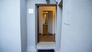A narrow hallway with a wooden floor, a doormat, and a light fixture above the door. - B&B Anele (Morano Calabro)