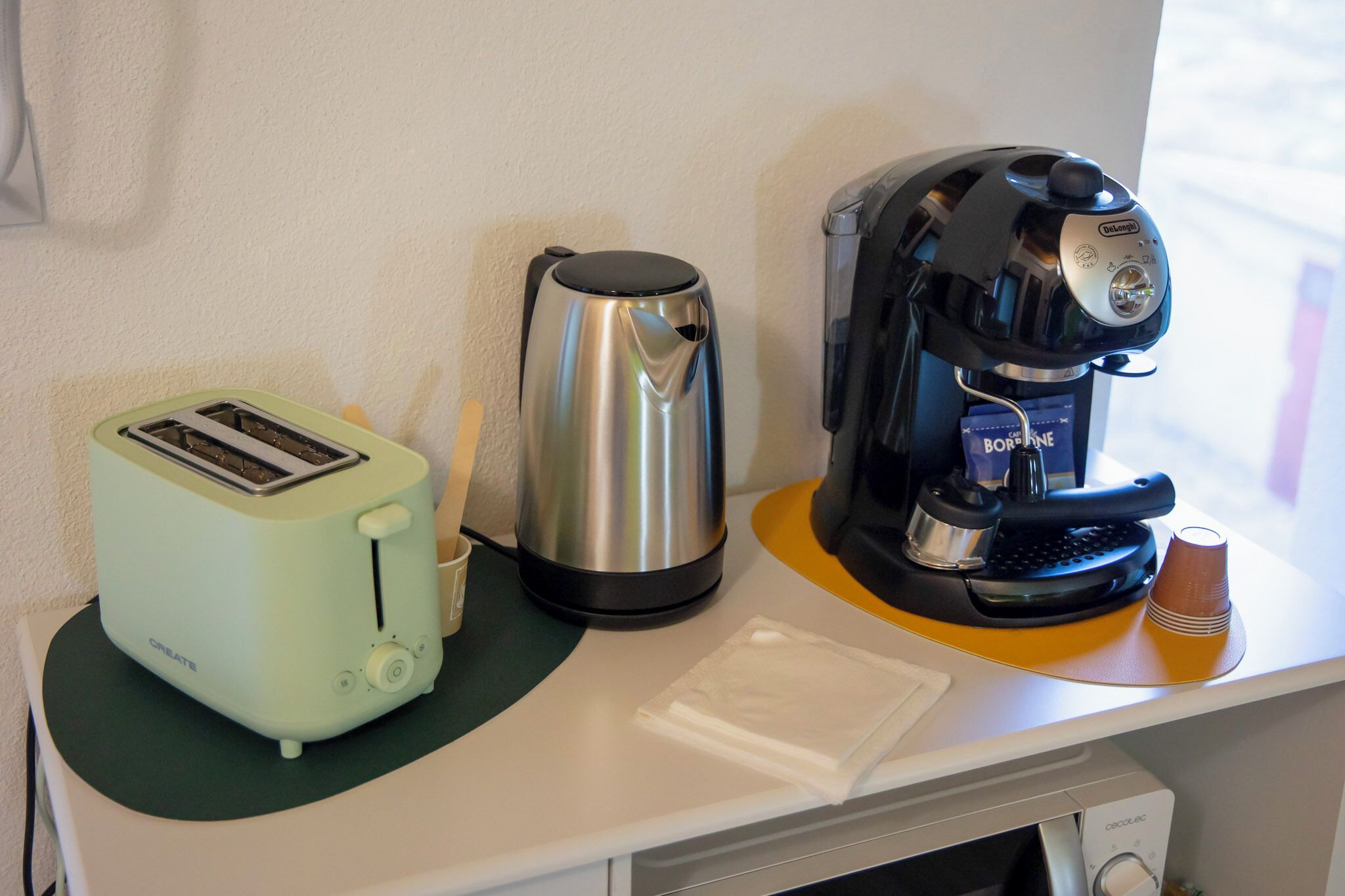 Een kitchenette met een broodrooster, een koffiezetapparaat en een waterkoker op een aanrecht.