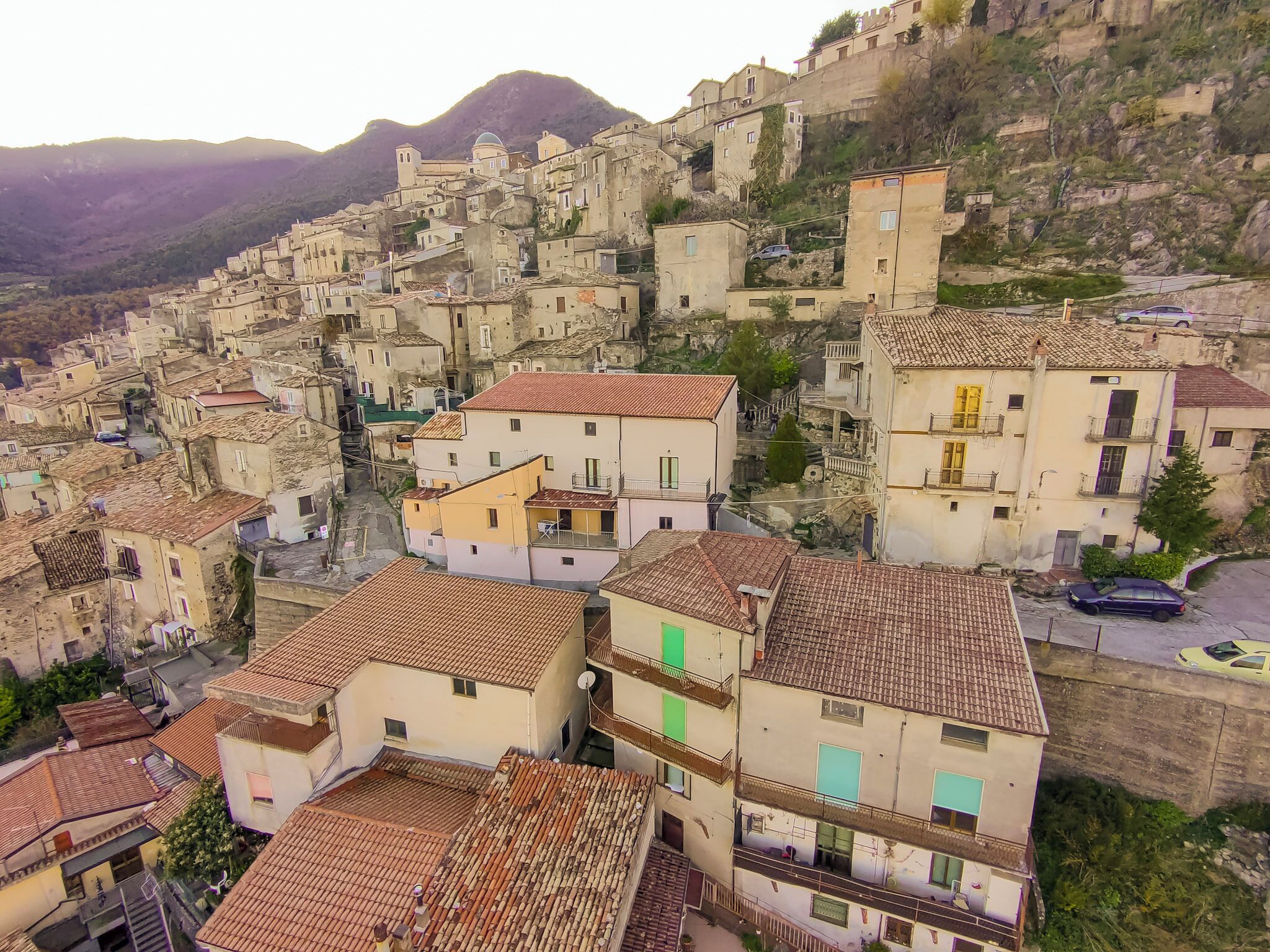 Un pueblo en una ladera con casas de techos de teja rojiza, calles estrechas y una montaña destacada al fondo.