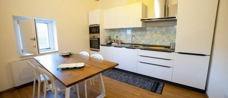 A modern kitchen with white cabinets, a wooden dining table, and a window.