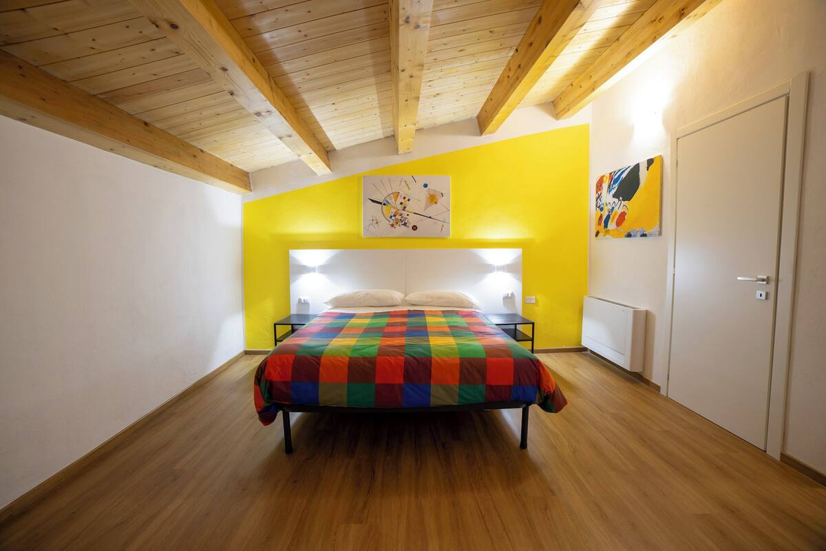 Ein Schlafzimmer mit Holzboden, einer farbenfrohen Bettdecke mit Schachmuster und zwei Wandleuchten.