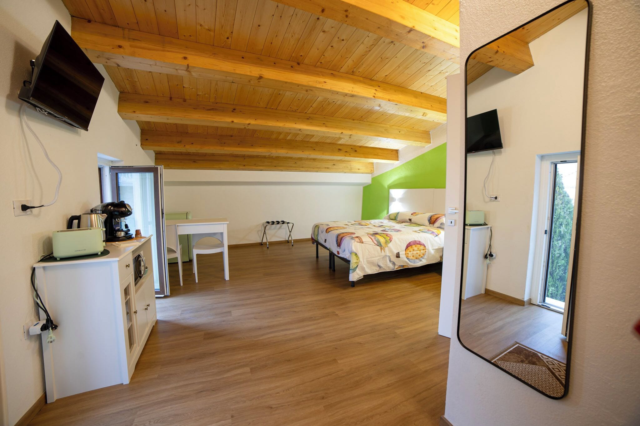A bedroom with a bed, a desk, a chair, a television, and a mirror.