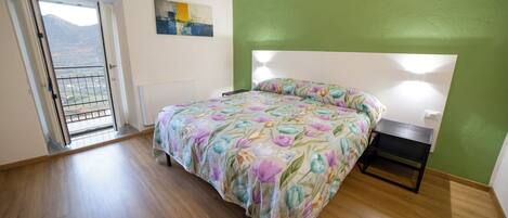 Quarto com cama, mesa de cabeceira, uma cadeira, um quadro e vista através de uma porta.