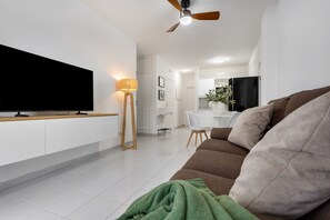 Een moderne woonkamer met een flatscreen televisie, een bank, een vloerlamp en een plafondventilator.