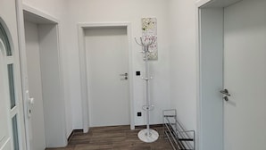 En hall med trägolv, vita väggar och en taklampa. Det finns dörrar på båda sidor, en klädhängare och en liten hylla.